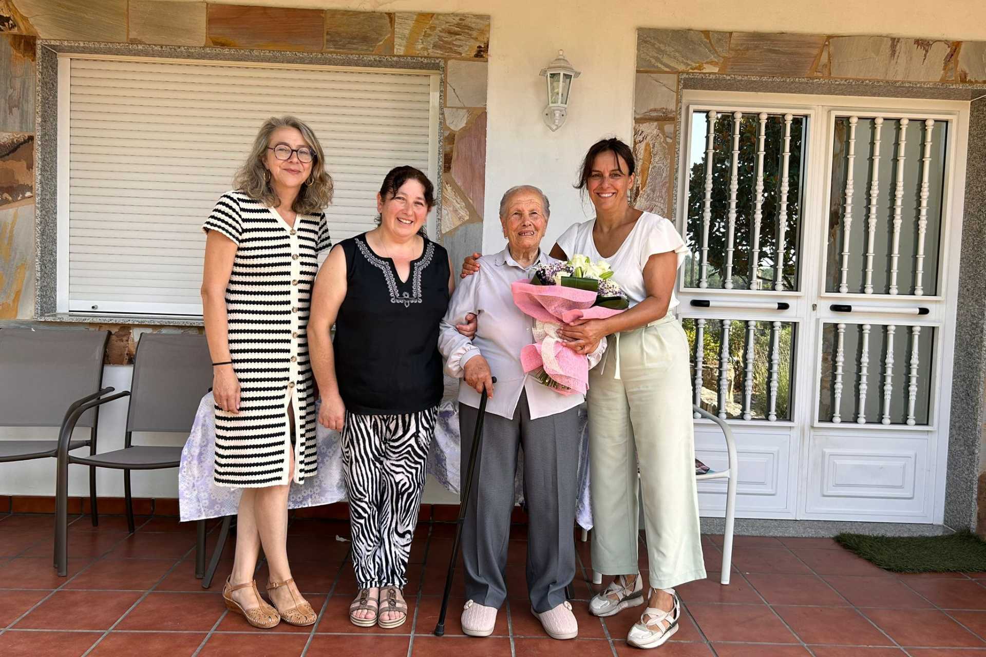 A alcaldesa agasalla cun ramo de flores a Amparo González, que soprou as 101 velas dende a parroquia de Vilar